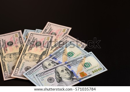 Banknotes of 50 and 100 dollars, lying in a fan shape on a black surface, free space