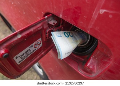Banknotes (euro) in the fuel filler of a red car. A fuel tank consumes money. Fuel prices increase causing money to be sucked into fuel tanks. 