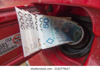 Banknotes (Polish zlotys) in the fuel filler of a red car. A fuel tank consumes money. Fuel prices increase causing money to be sucked into fuel tanks. 