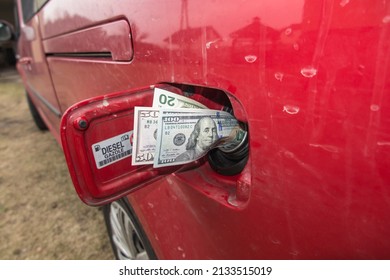 Banknotes (US dollars) in the fuel filler of a red car. A fuel tank consumes money. Fuel prices increase causing money to be sucked into fuel tanks.