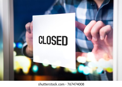 Bankruptcy, Failed Business Going Down Or Opening Times Concept. Man Putting Closed Sign In Window In Cafe, Restaurant, Shop, Store Or Agency. Late At Night In City.