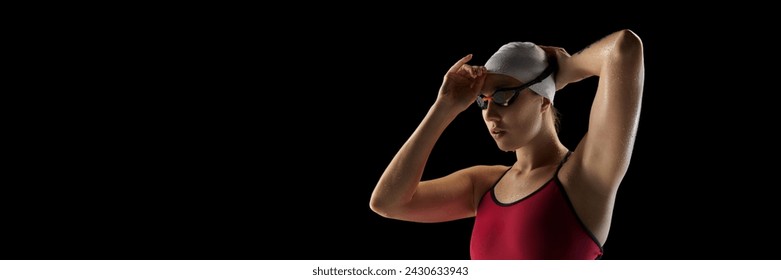 Banner. Athletic of young female swimmer wearing cap and goggles before swim race against black studio background. Negative space. Concept of professional sport, motion, strength and power. Ad - Powered by Shutterstock