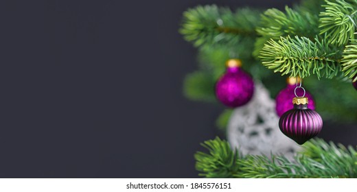 Banner with beautiful purple glass tree bauble on decorated Christmas tree with other seasonal tree ornaments on dark black background with empty copy space