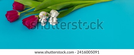 Banner with bouquet of burgundy tulips and toy angels talking. Turquoise, cyan background. Copy space, space for text. Valentine's Day, Easter.