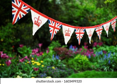 Banner of British Union Jack flag and royal crown celebratory bunting hanging in front of a bright English summer garden background - Shutterstock ID 1603499320