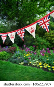 Banner Of British Union Jack Flag And Royal Crown Celebratory Bunting Hanging In Front Of A Flowery English Summer Garden Background