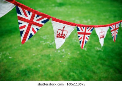 Banner Of British Union Jack Flag And Royal Crown Celebratory Bunting Hanging In Front Of A Bright Green English Summer Background