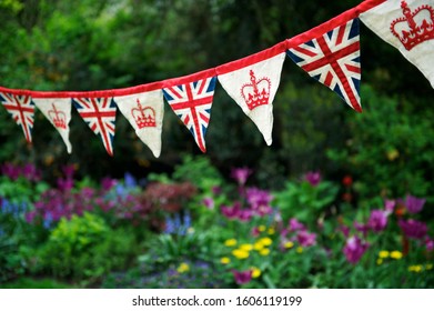 Banner Of British Union Jack Flag And Royal Crown Celebratory Bunting Hanging In Front Of A Flowery English Summer Garden Background