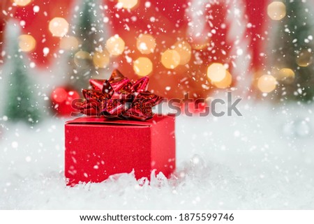 Banner. Christmas red gift box in a red snowy landscape on a bokeh background. Space for text. The concept of the delivery of gifts and greetings card happy New year. Close up.