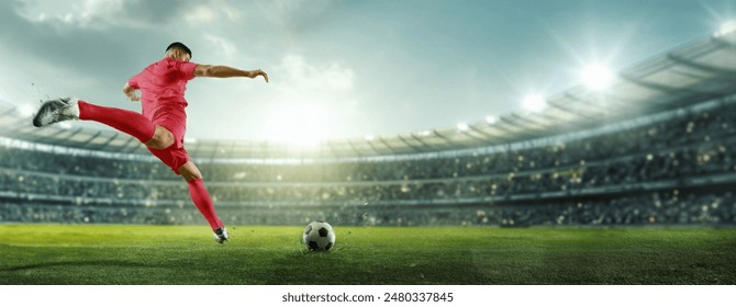 Banner. Cinematic view. Soccer player in red strikes ball with power, aiming for goal in brightly lit stadium filled with spectators. Concept of sports games, competition, championship, tournament. Ad - Powered by Shutterstock