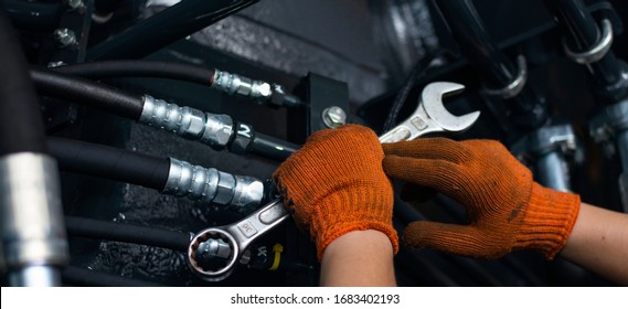 Banner with close up view of hydraulic pipes of heavy industry machine and hands of mechanic. Low key. Hydraulic maintenance concept.