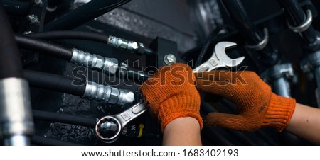 Banner with close up view of hydraulic pipes of heavy industry machine and hands of mechanic. Low key. Hydraulic maintenance concept.