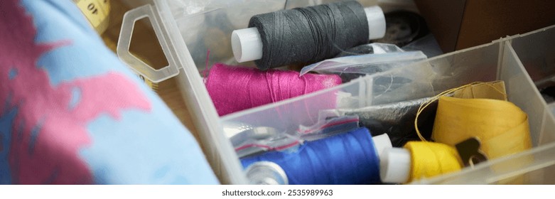 Banner of container with several multi-color thread bobbins, rolled measuring tape, button and small cellophane packets - Powered by Shutterstock