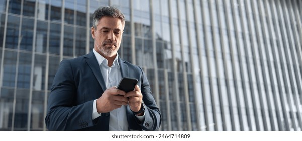 Banner with copy space mature hispanic senior business man using smartphone cellphone at office building. Focused serious latin middle age entrepreneur businessman holding mobile cell phone for work - Powered by Shutterstock