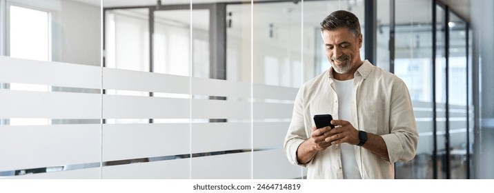 Banner with copy space. Smiling 40s mature Latin or Indian businessman holding smartphone in office. Middle aged manager man using cell phone mobile app. Digital technology application for business. - Powered by Shutterstock