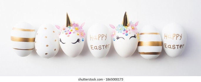 Banner. Easter eggs in the form of a unicorn, and with a gold pattern on a white background. Flat lay. Copy space for text. 