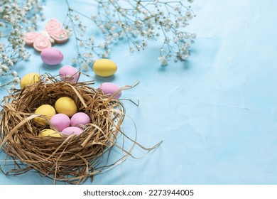 Banner for the Easter holiday. Colored eggs in a straw nest and white spring flowers on a blue background. Place for text. Top view. - Powered by Shutterstock