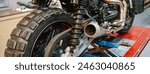 Banner of of exhaust pipe and shock absorber of custom motorbike on factory. Close up of vintage scrambler motorcycle over platform ready to review on mechanic garage.