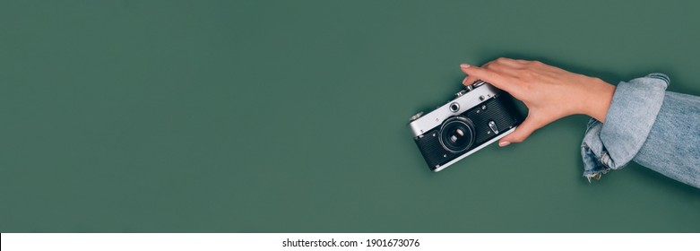 Banner with female hand holding old vintage photo camera on green background with copy space for text. Trendy vintage photography, Online photography school concept, selective focus