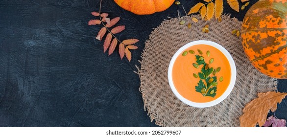 banner with flat lay of pumpkin soup next to yellow leaves, pumpkins and napkin on black texture background. warming hearty soup on a cold autumn day. rustic style. copy space - Shutterstock ID 2052799607