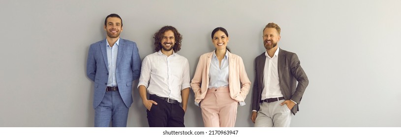 Banner With Group Portrait Of Happy Confident Corporate Employees Looking At Camera And Smiling. Team Of Four Positive Young Business People In Smart Office Wear Standing Together Against Studio Wall