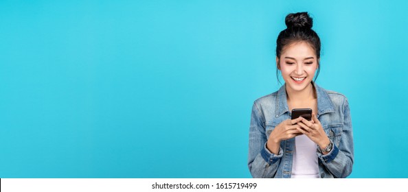 Banner of Happy asian woman feeling happiness and standing typing smartphone on blue background. Cute asia girl smiling wearing casual jeans shirt and connect internet shopping online and surfing.