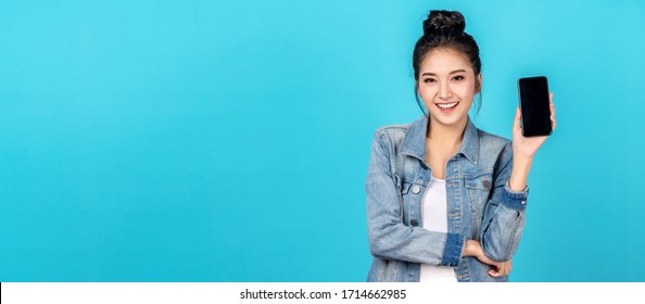 Banner Of Happy Asian Woman Feeling Happiness And Standing Hold Smartphone On Blue Background. Cute Asia Girl Smiling Wearing Casual Jeans Shirt And Connect Internet Shopping Online And Present