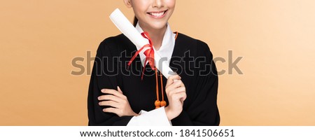 Banner of Happy Graduate asian woman in cap and gowm holding Certificated or diploma on Beige background,Graduation Concept