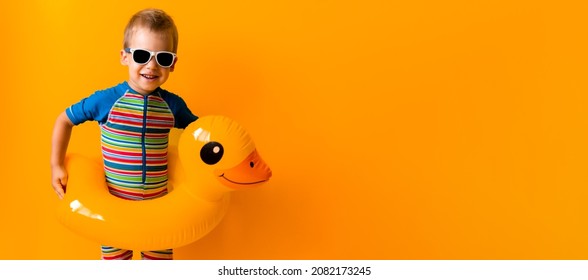 banner happy little smiling child swimmer sport boy wear sun glasses swimsuit, Kid Inflatable swimming ring yellow duck point to side away, isolated orange background. hot summer vacation copy space