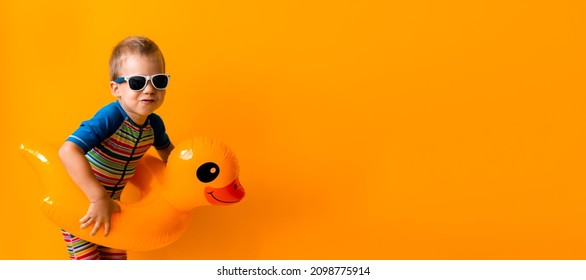 Banner Happy Little Smiling Child Swimmer Sport Boy Wear Sun Glasses Swimsuit, Kid Inflatable Swimming Ring Yellow Duck Point To Side Away, Isolated Orange Background. Hot Summer Vacation Copy Space