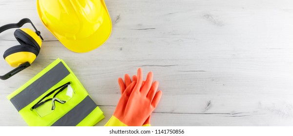 Banner image of construction safety gear including a hard hat, folded reflective jacket, goggles, and rubber gloves flat lay on white wooden surface with copy space - Powered by Shutterstock