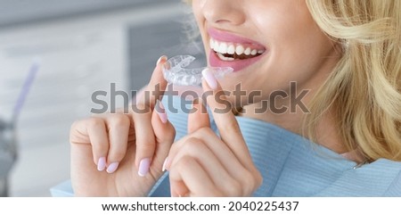 Banner for invisalign orthodontics, modern dentistry concept. Unrecognizable blonde woman with healthy white teeth holding invisible braces while sitting at dental chair, closeup portrait, copy space