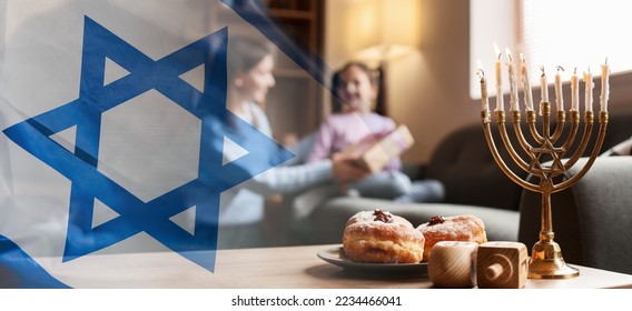 Banner with Israeli national flag and menorah, dreidels and donuts on table of happy family celebrating Hannukah at home
