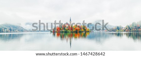 Banner of lake Bled in Slovenia. Charming autumn panorama landscape of island with church rounded colorful trees in the middle of Bled lake. Colorful autumn scenery, popular travel destination.