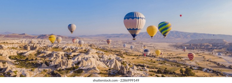 BANNER, LONG FORMAT Colorful hot air balloons flying over at fairy chimneys valley in Nevsehir, Goreme, Cappadocia Turkey. Spectacular panoramic drone view of the underground city and ballooning