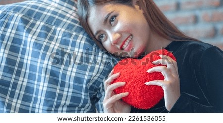 banner of Lover couple happy in love relaxing on sofa looking in eye smiling teasing with big red heart shape pillow in valentine day honeymoon. teasing teasing with red heart pillow.