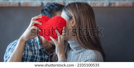 banner of Lover couple happy in love relaxing on sofa looking in eye smiling teasing with big red heart shape pillow in valentine day honeymoon. teasing teasing with red heart pillow.