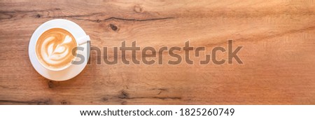 Banner made from cappuccino with frothy foam, white coffee cup top view closeup on wooden background. Flat lay style.