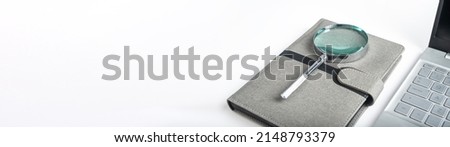 Banner with magnifying glass at notebook and open laptop. Schedule, agenda analysis, thorough planning. Copy space. High quality photo