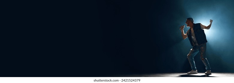 Banner. Man, artist singing with microphone in smoke illuminated blue stage light against dark background with negative space for text. Concept f music and dance, lifestyle, festivals, concerts. Ad - Powered by Shutterstock