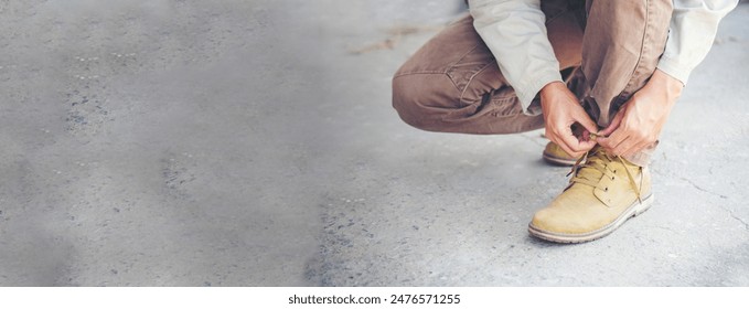 Banner Man kneels down rope tie shoes industry boots for worker. Close up shot of man hands tied shoestring for his brown construction boots. Close-up man hands tie up footwear shoes with copy space - Powered by Shutterstock