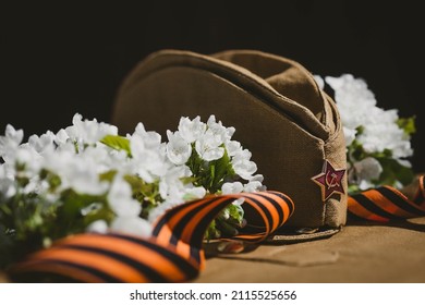 Banner For May 9. A Military Uniform, A Cap With A Star, A St. George Ribbon And A Cherry Blossom In The Background. The Concept Of The Great Victory Day 941-1945 And Defender Of The Fatherland Day.