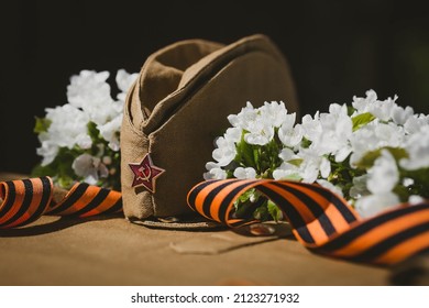 Banner For May 9. A Military Uniform, A Cap With A Star, A St. George Ribbon And A Cherry Blossom In The Background. The Concept Of The Great Victory Day 941-1945 And Defender Of The Fatherland Day.