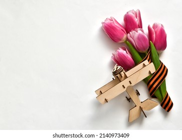 Banner For May 9. Pink Tulips, St. George Ribbon And Wooden Plane On A White Background. The Concept Of The Great Victory Day 941-1945 And Defender Of The Fatherland Day. Flat Lay, Copy Space 