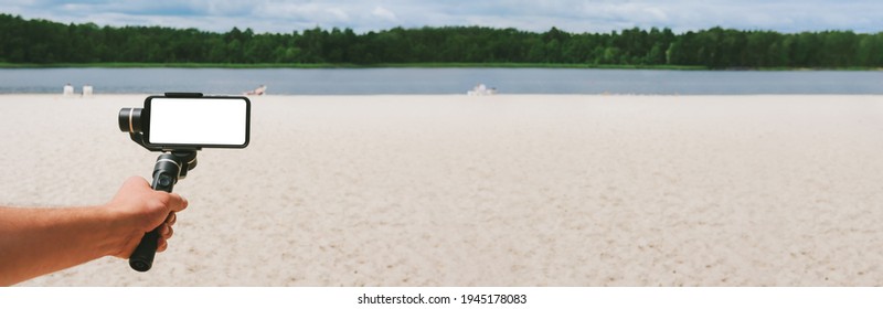 Banner, Mockup of a smartphone on a Steadicam in a man's hand. Against the backdrop of a sand beach and nature with a lake - Powered by Shutterstock