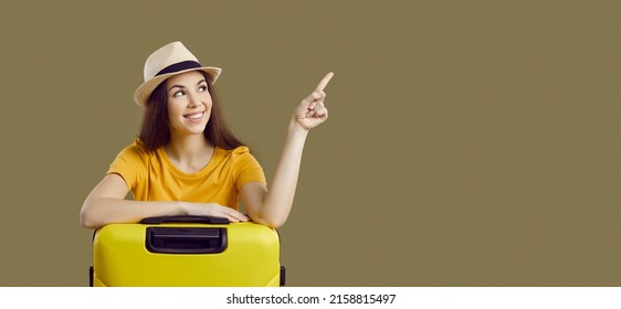 Banner narrow wide shot of smiling young Caucasian woman isolated on green studio background hold suitcase point at empty copy space. Happy girl recommend good travel sale offer or vacation deal.