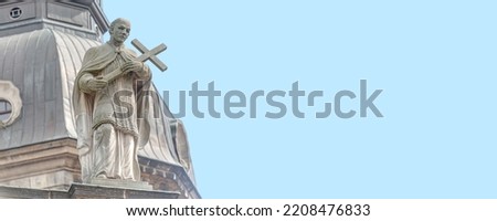 Banner with old roof statute of priest or monk holding a big cross at Cathedral of Holy Trinity, historical center of Dresden, Germany, at blue sky solid background with copy space