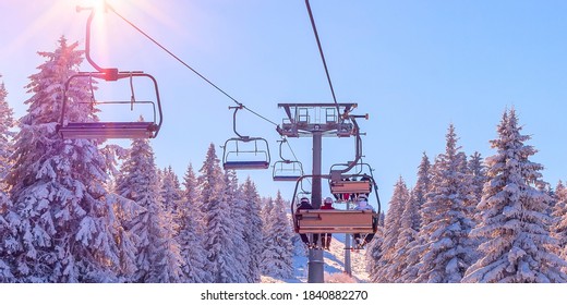 Banner panorama of ski resort, skiers on the ski lift, white snow pine trees at pink sunset or dawn, Kopaonik, Serbia