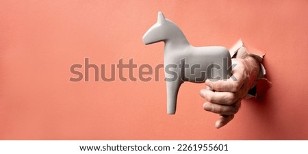 a banner with a paper background through a hole in which a hand with a horse breaks through. trojan horse trick gift