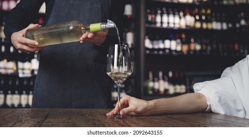 Banner photo waiter pouring white wine into glass goblet to young woman.